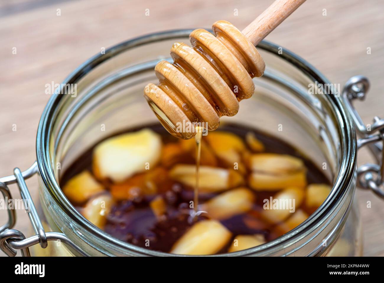 Garlic with honey in a glass jar on the kitchen counter with a wooden honey stick Stock Photo