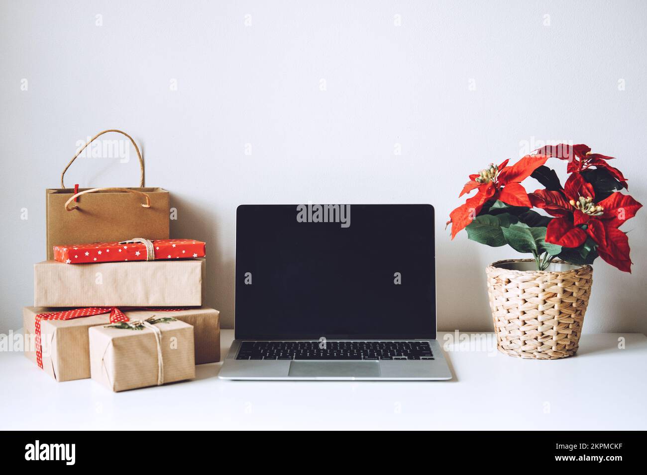 Blank display screen laptop computer with Poinsettias Christmas Flower and gift boxes on white table. Home office desk workspace with Mock up copy Stock Photo