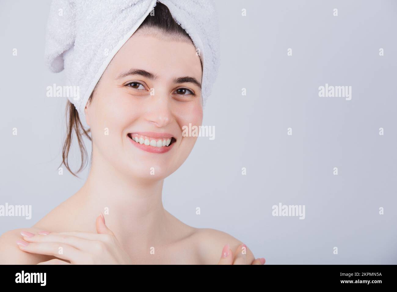 Young Woman With Towel On Head Smiling to Camera. Body Care Concept. Young girl drying hair with towel on head after shower treatment. Stock Photo