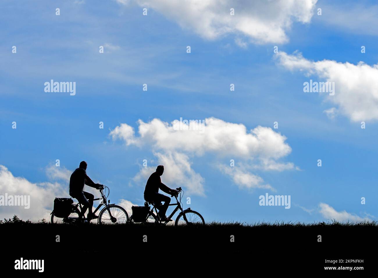 Two elderly cyclists silhouetted riding their bicycles against cloudy sky in summer Stock Photo