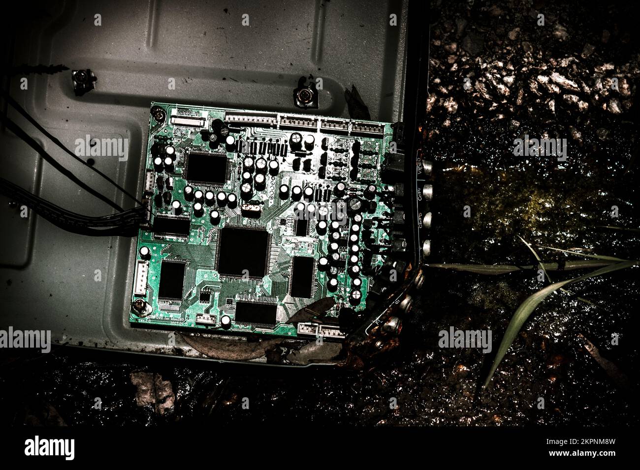 Green circuit board from a broken computer laying scattered in a gutter