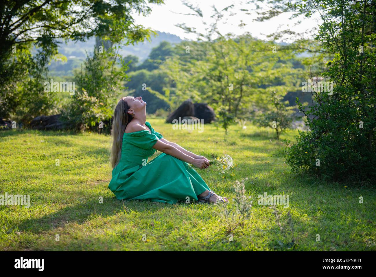 a woman is sitting on the grass with flowers in a green dress Stock ...