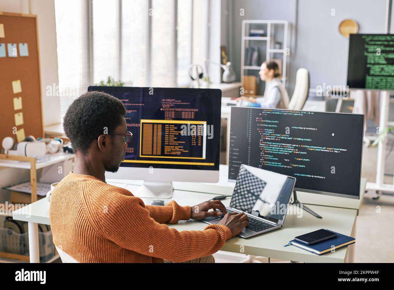 Young man in warm sweater coding on laptop in office of IT company Stock Photo