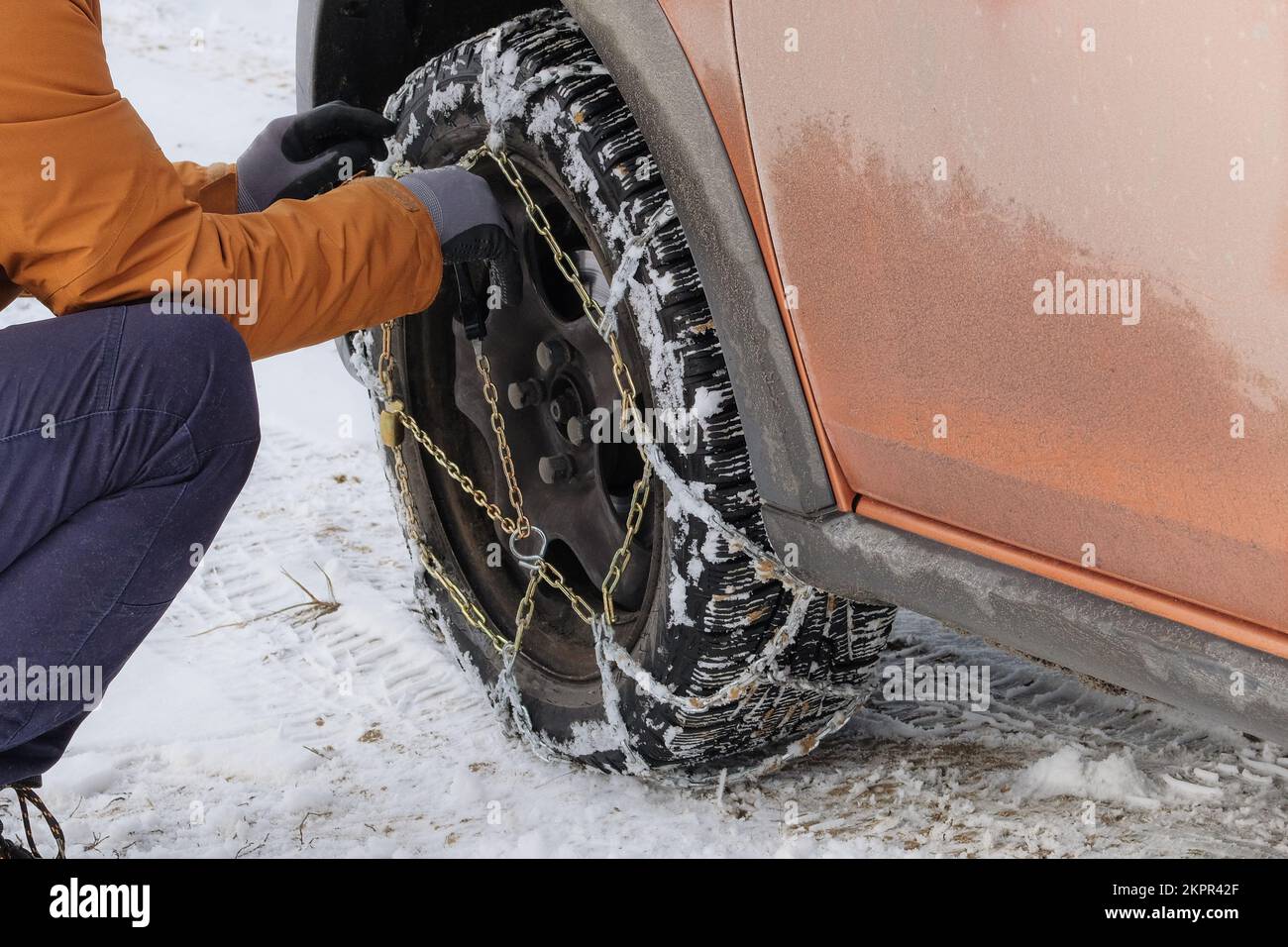 Driver installs chains on the wheel of his car in winter. Vehicle