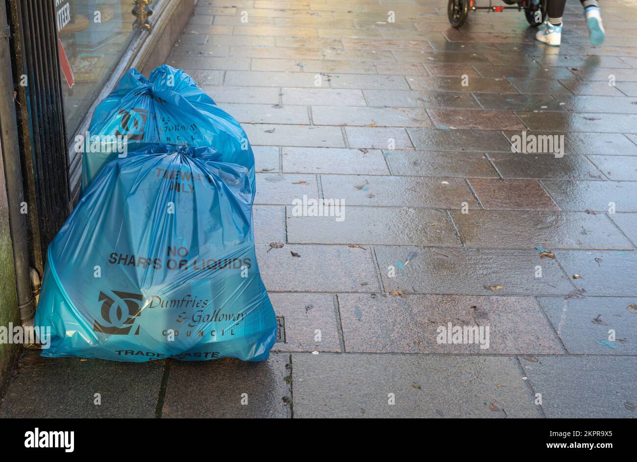 Commercial trade waste put outside a shop in the town centre of Dumfries, Scotland, for collection by refuse disposal teams, people walking past. Stock Photo