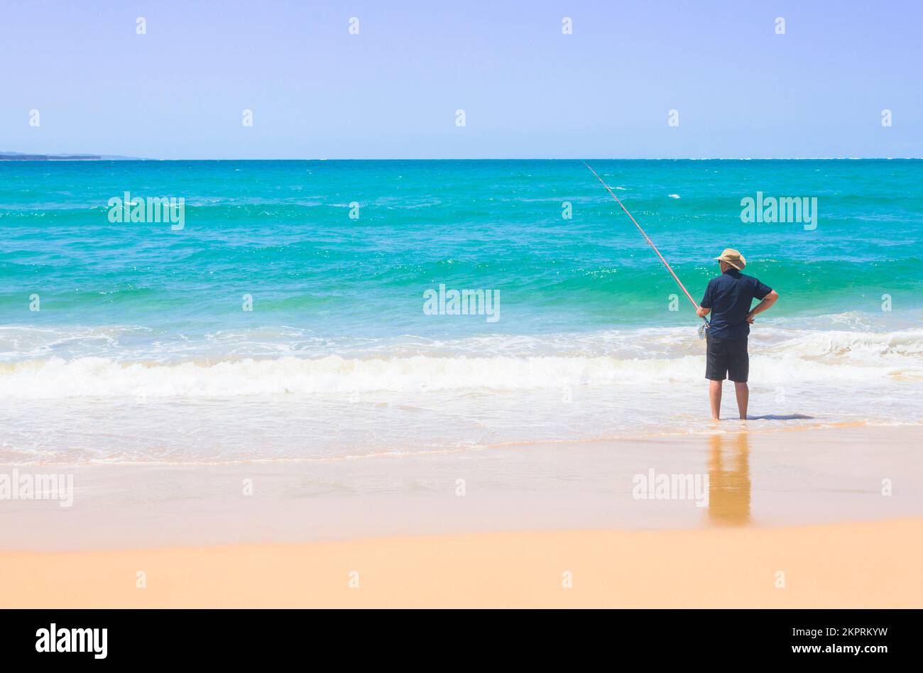 Travel and lifestyle photography on a male fisherman holding rod at tropical surf beach. Taken: Amity Point, North Stradbroke Island, Queensland, Aust Stock Photo