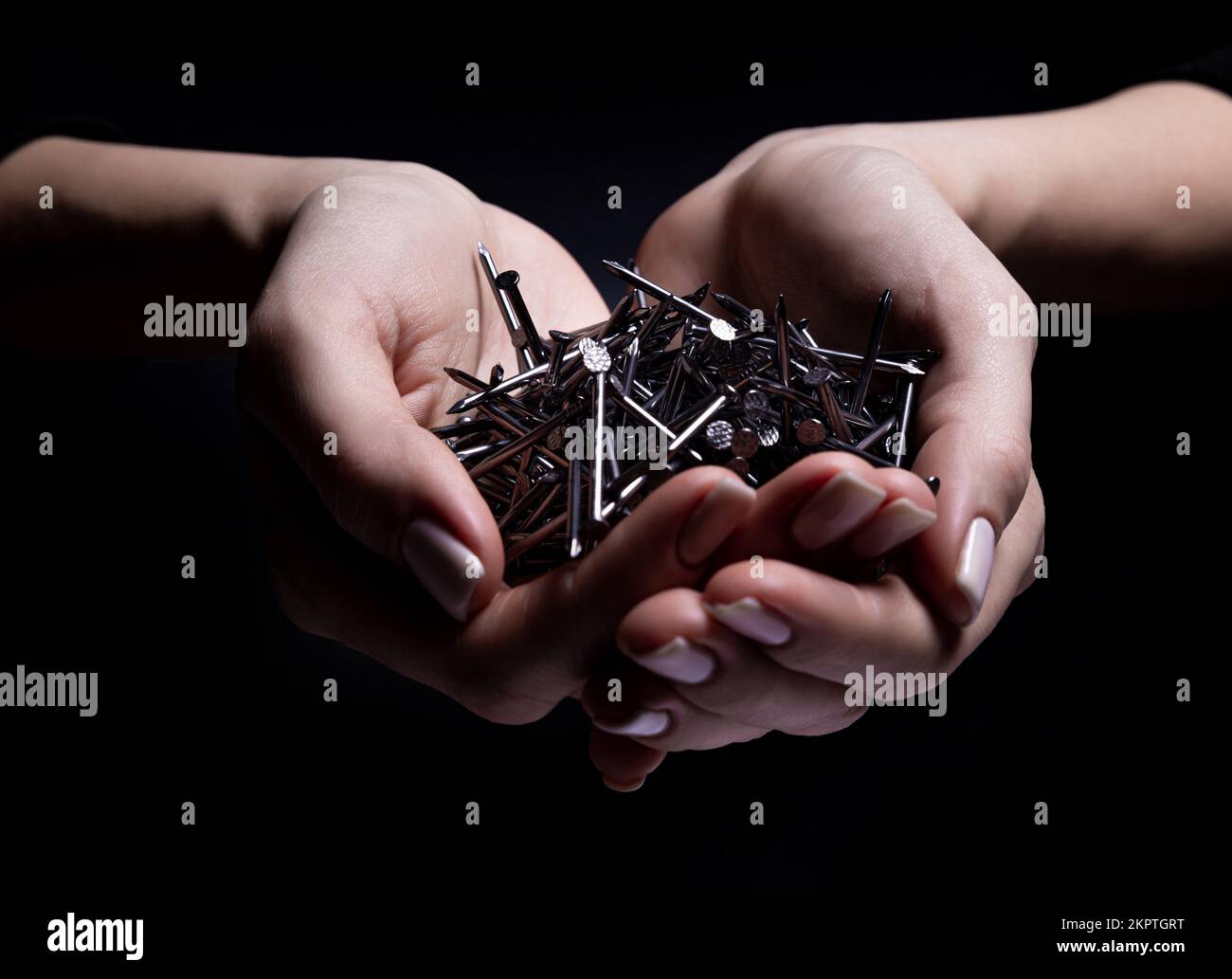Woman's hands holding screws and dowels in palms. Isolated on black. female hands hold screws nails washers nuts on a black background Stock Photo