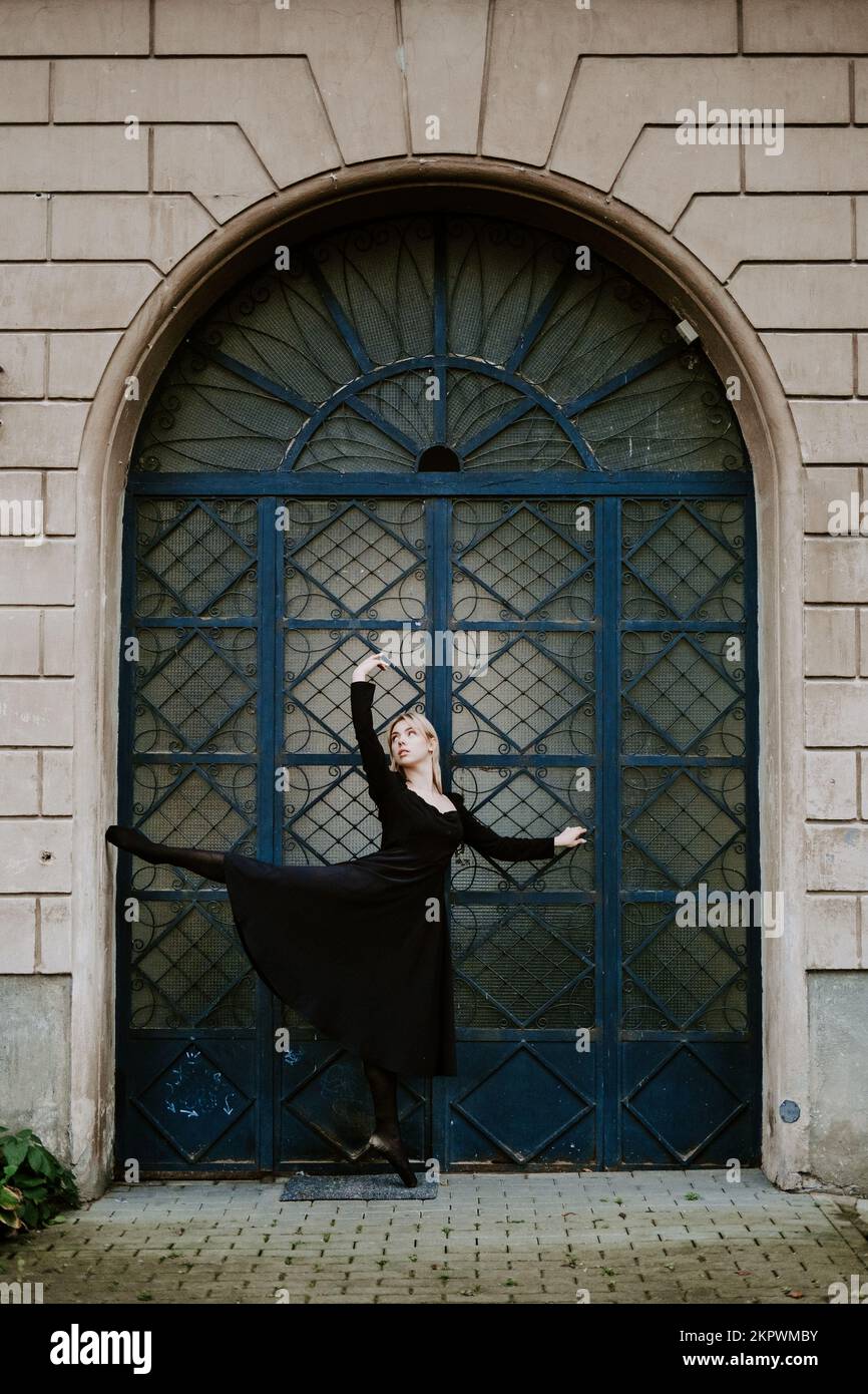 Ballerina Dancing in autumn city street, Modern Ballet Dancer in black dress, Pointe Shoes outdoors. Ballerina stretches, daily ballet stretching Stock Photo