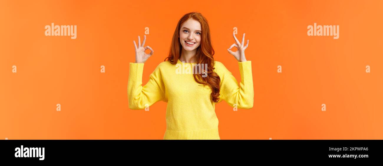 Perfect idea concept, acception. Good-looking redhead girl in yellow sweater, showing okay, good or approval sign smiling nod agreement, satisfied Stock Photo