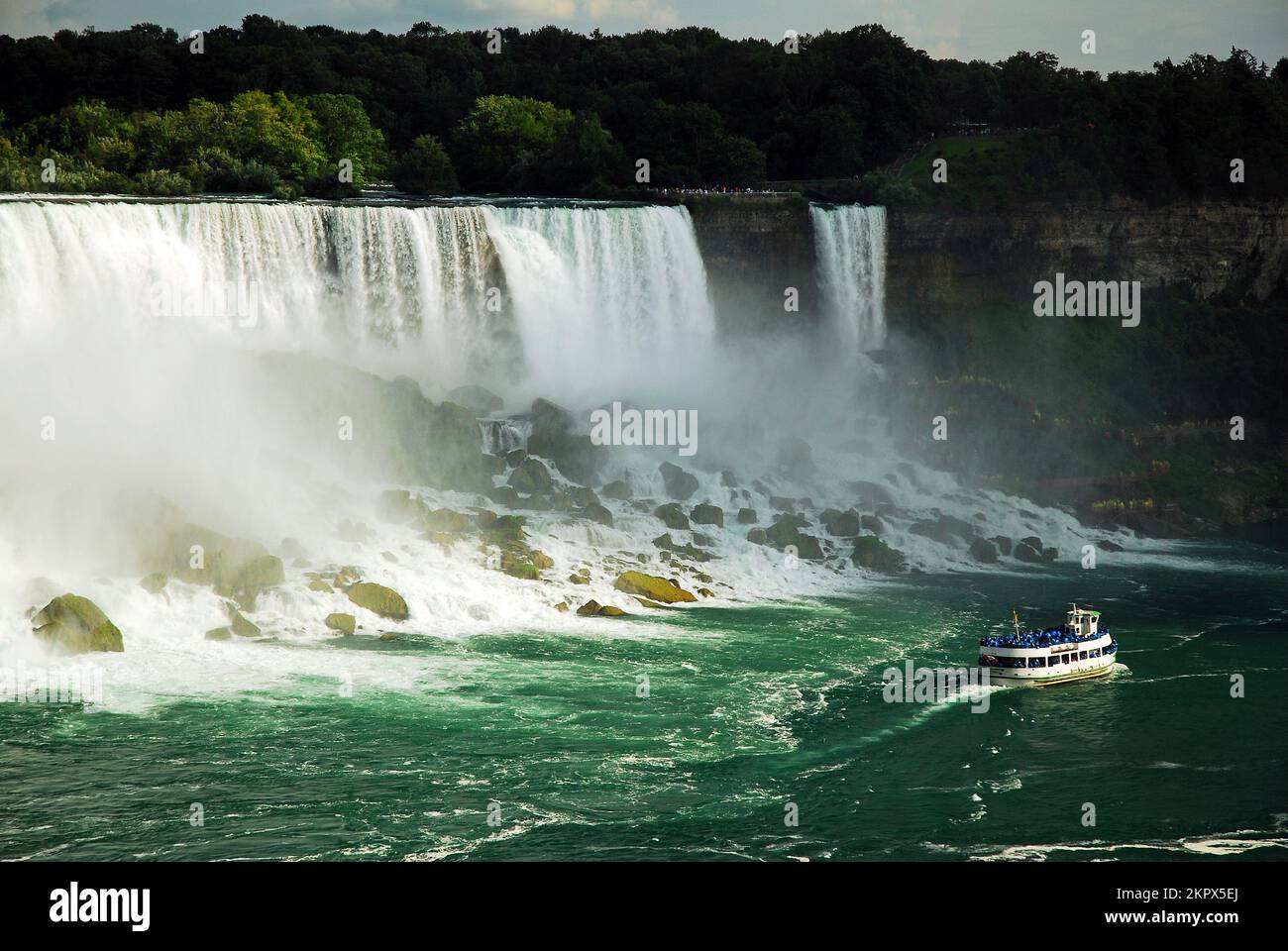 The Maid of the Mist tour boat cruises past American Falls in Niagara Falls Stock Photo