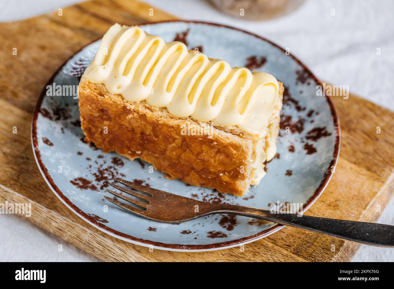 French dessert called Mille Feuille or Napoleon cake on rustic wooden board. Layered tasty cake with vanilla cream and puff pastry. Stock Photo