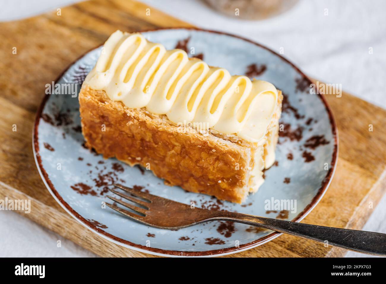 French dessert called Mille Feuille or Napoleon cake on rustic wooden board. Layered tasty cake with vanilla cream and puff pastry. Stock Photo