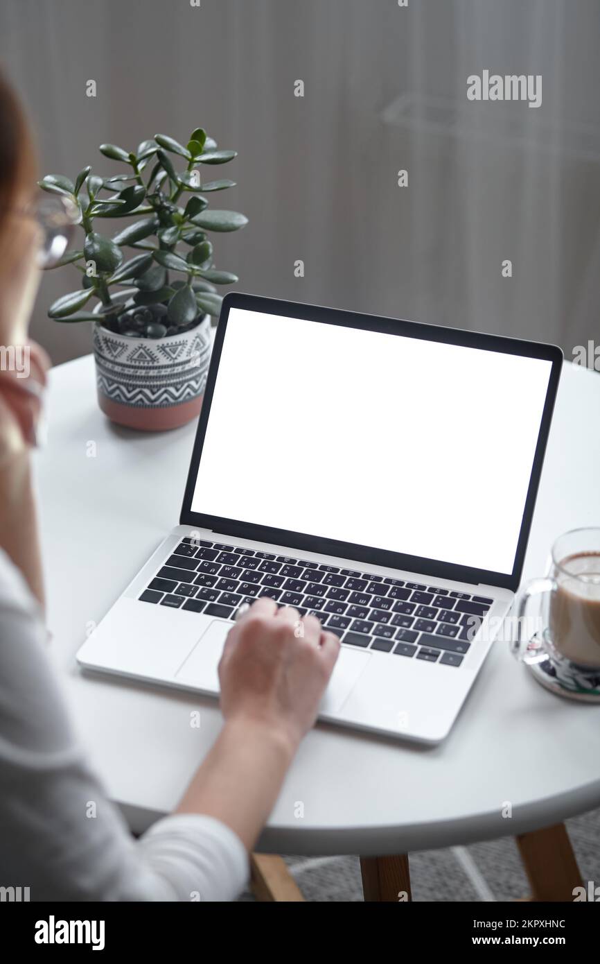 Mockup white screen laptop woman using computer while sitting at table at home, back view Stock Photo
