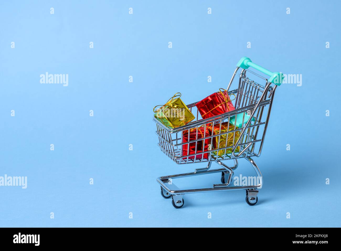 Close up of a small shopping cart full of colourful Christmas gifts on a blue background. Copy space. Stock Photo
