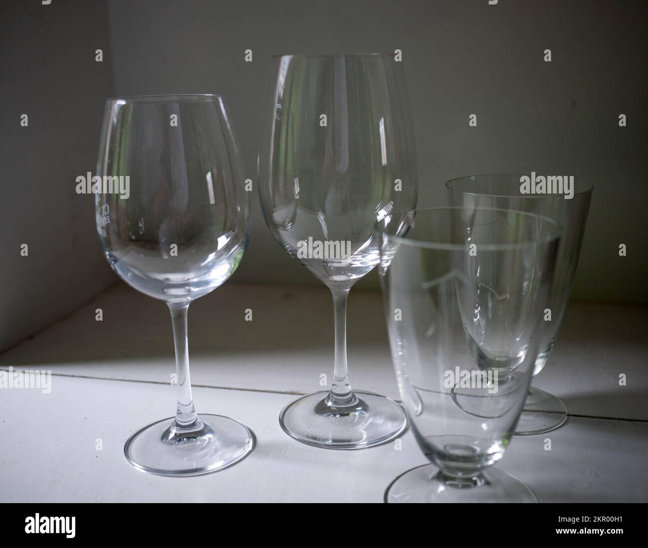 Clear glassware on a white cupboard shelft with a dark back ground.  Wine glasses and Pilsner Tulip glasses. Stock Photo