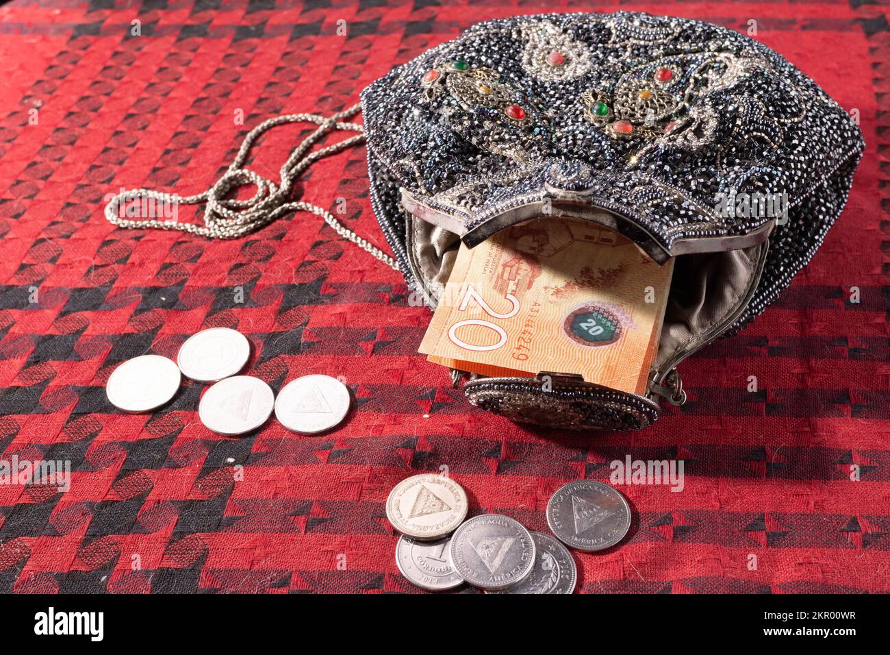 Beaded antique purse with Nicaraguan currency and coins on a red and black textile background, bought in the US in the 1980s. Stock Photo