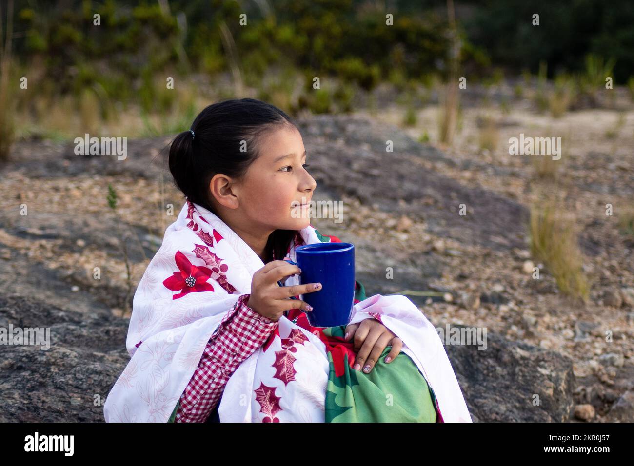 indigenous girl celebrating christmas with  in the forest drinking coffee sitting on a stone Stock Photo