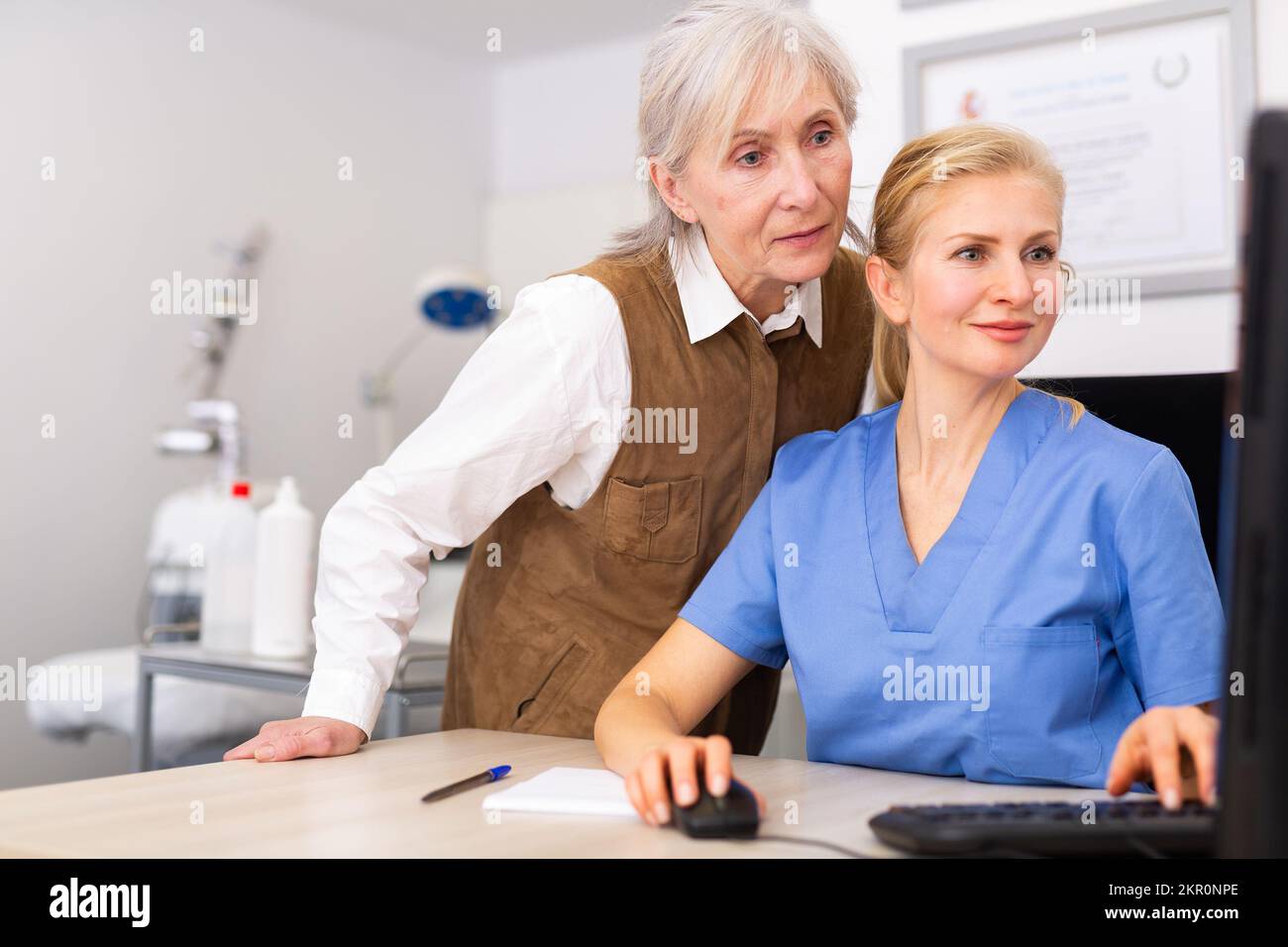 Interested elderly female client with cosmetologist looking at computer screen Stock Photo