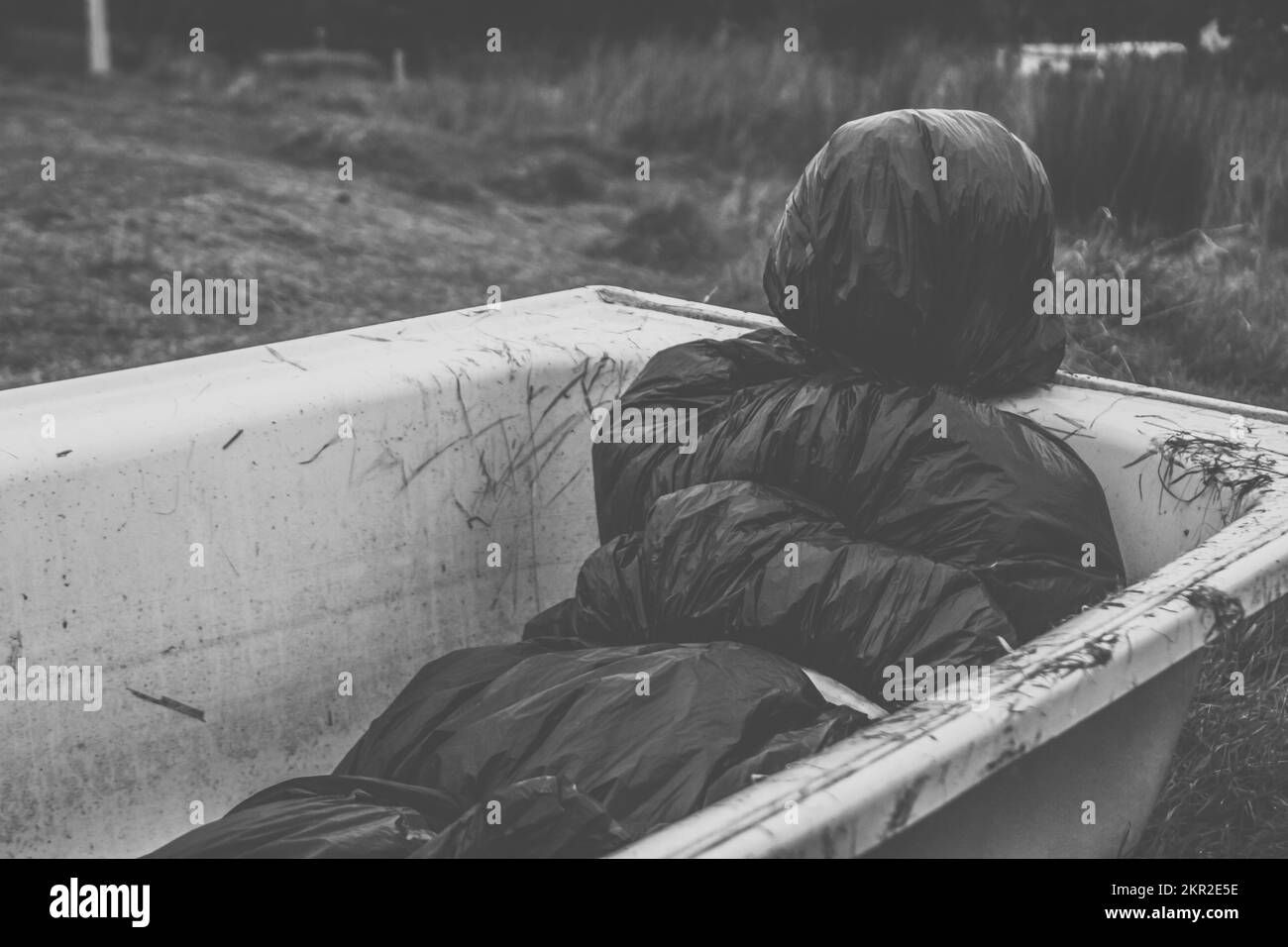Black and white image of dead body wrapped in plastic packaging placed in an empty bath tub on a dark ghostly gravesite, killing field – Crime scene i Stock Photo