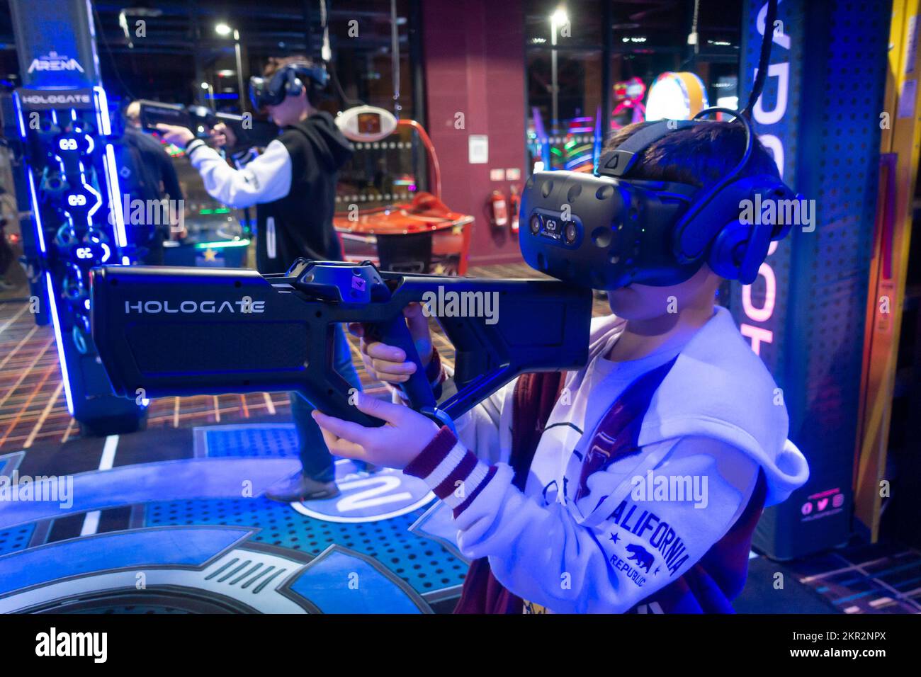 A boy playing a virtual reality video game in an arcade, holding a gun