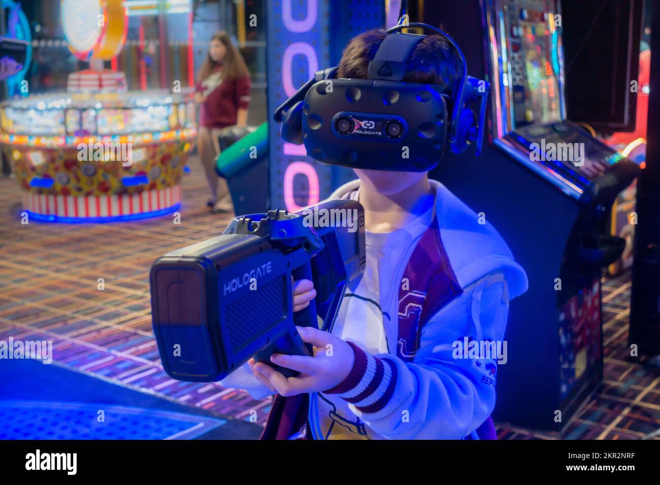 A boy playing a virtual reality video game in an arcade, holding a gun