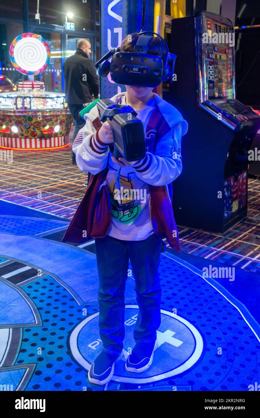 A boy playing a virtual reality video game in an arcade, holding a gun and wearing a VR headset Stock Photo