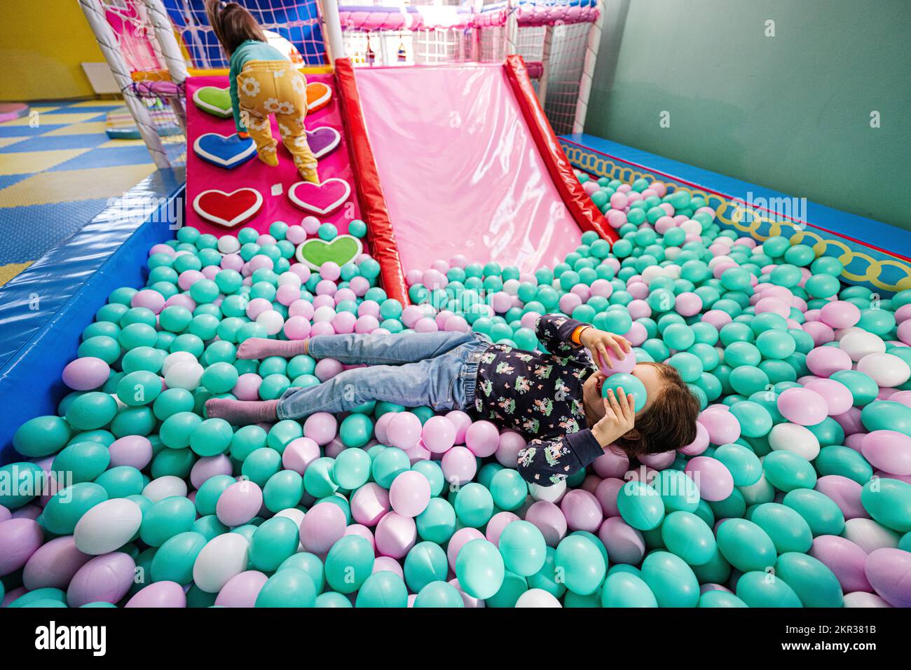 Happy sisters playing at indoor play center playground. Girl lying at color balls in ball pool