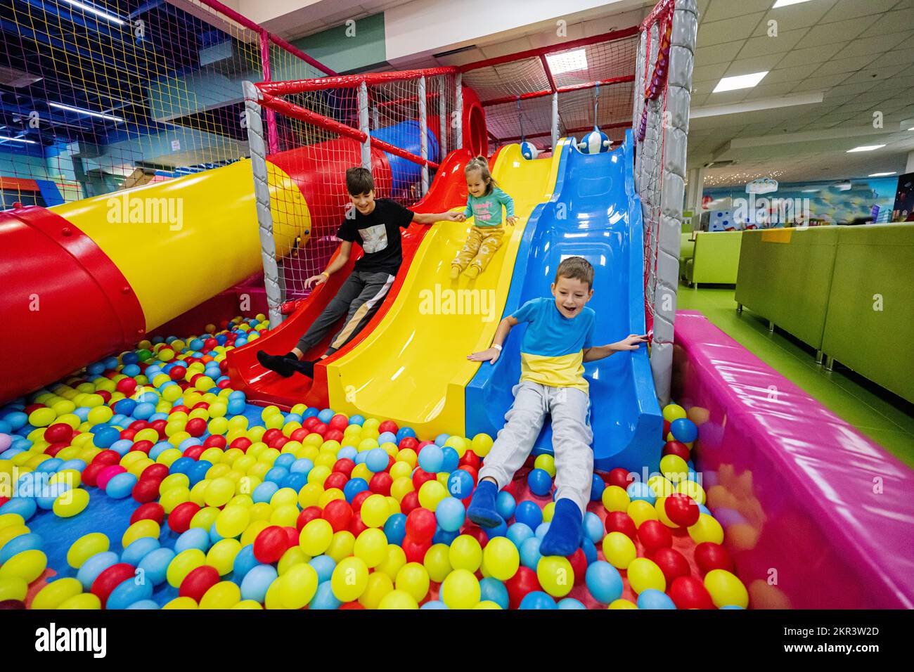 Happy kids playing at indoor play center playground. Children slides in colored slide into balls