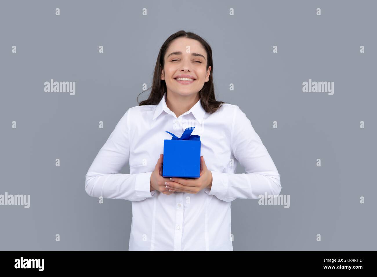 Happy birthday. Woman holding gift box with ribbon. Studio portrait over gray background. Stock Photo