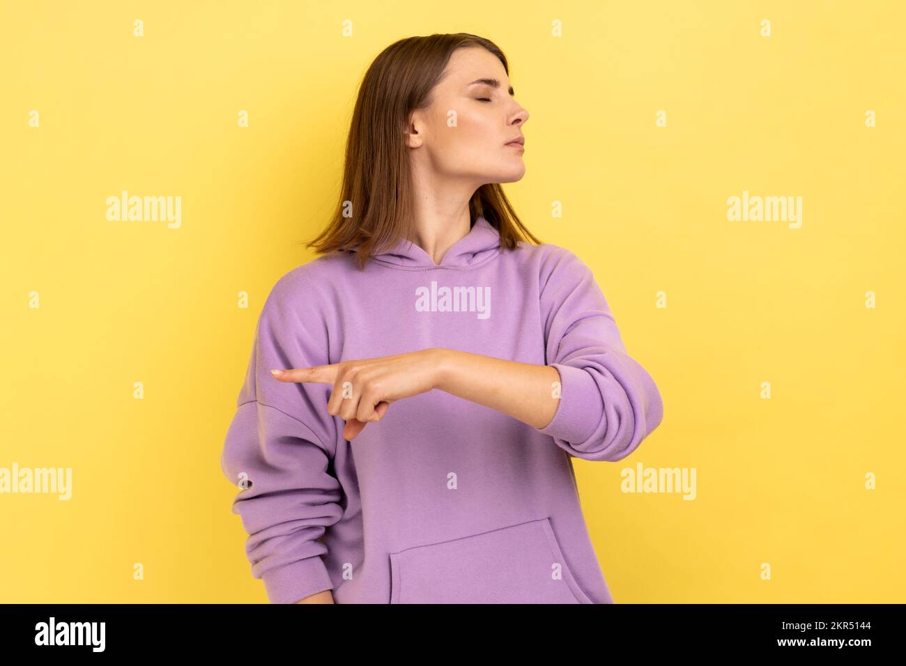 Get out. Portrait of upset vexed woman showing exit, demanding to leave her alone, has resentful irritated expression, wearing purple hoodie. Indoor studio shot isolated on yellow background. Stock Photo