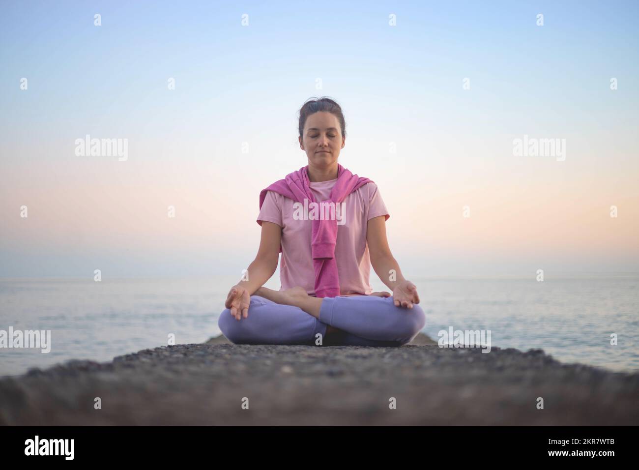 Yoga woman meditation in lotus position at pebble sea beach sunset sky ...