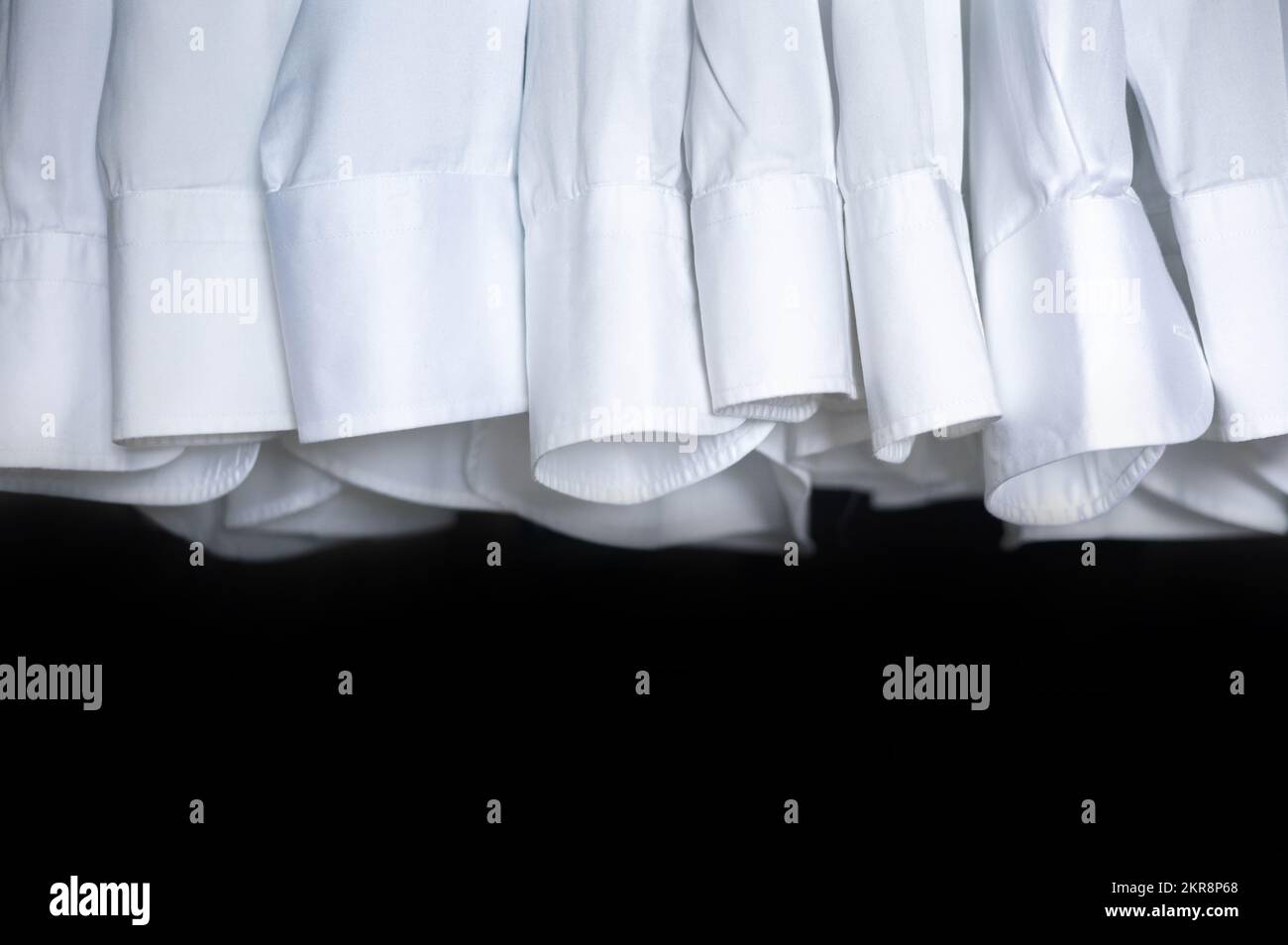 Male business wardrobe many clean white shirt sleeve hanging isolated on black background Stock Photo