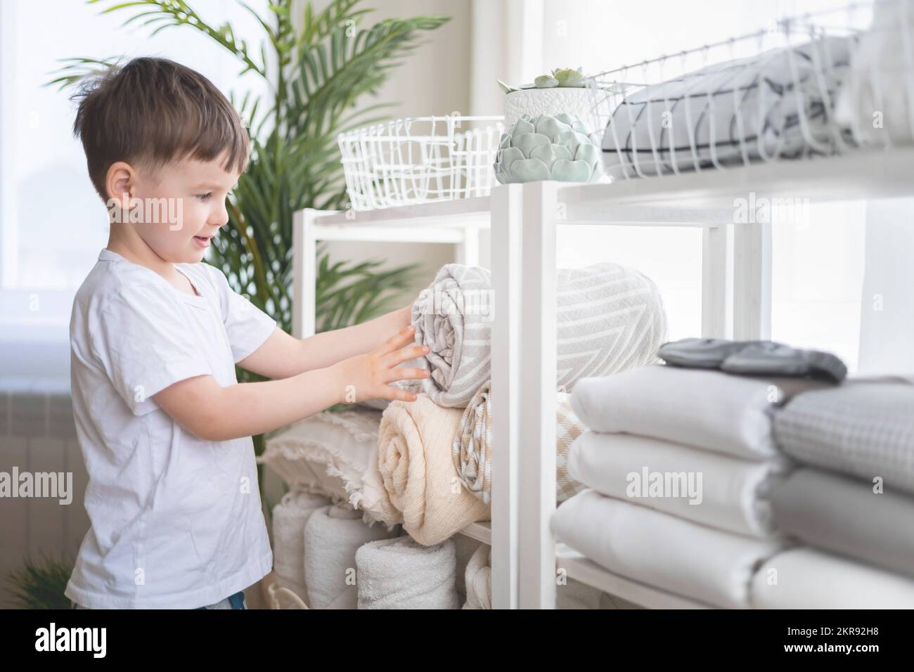 The child puts the bedding in a closet with neatly folded things. vertical storage. Stock Photo