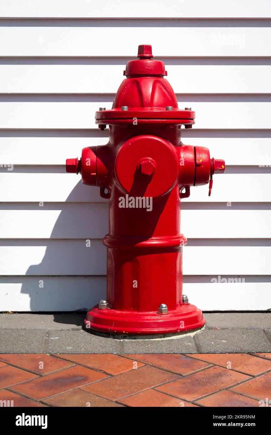 Red fire hydrant in front of white weatherboard wall, Cambridge, Waikato, North Island, New Zealand Stock Photo