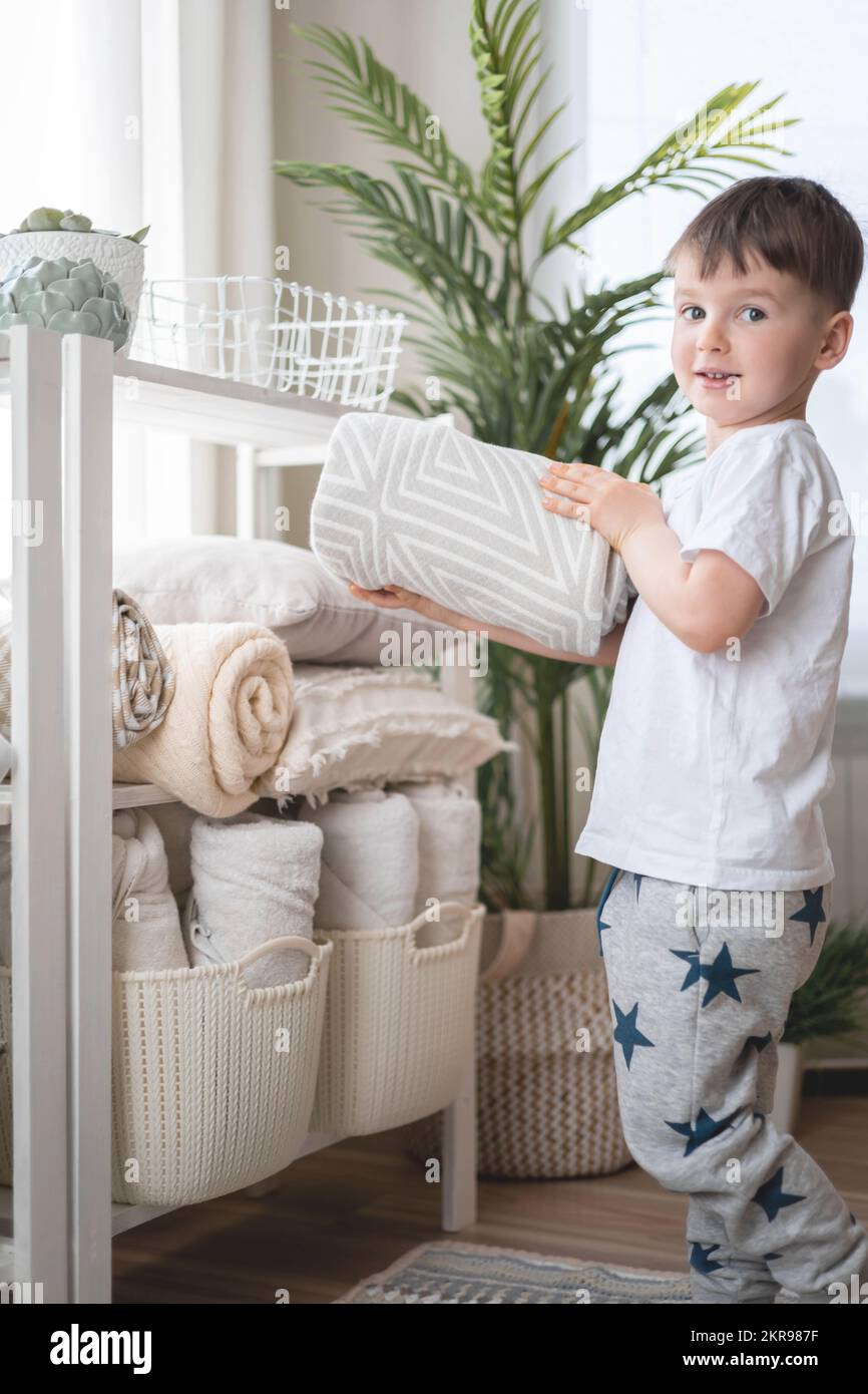 The child puts the bedding in a closet with neatly folded things. vertical storage. Stock Photo