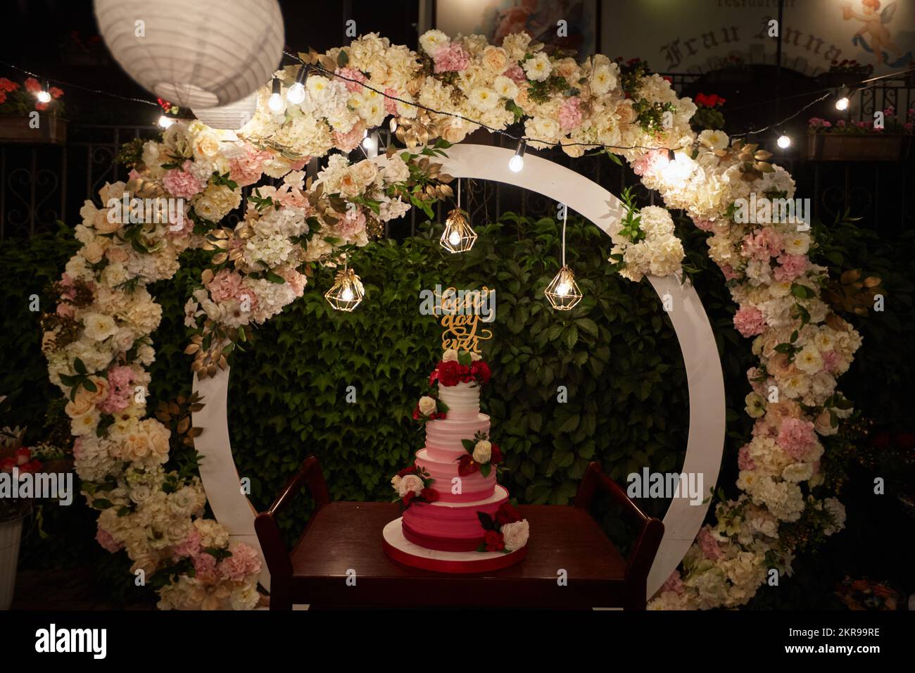 Wedding cake with best day ever sign on green garden decorated for wedding party at night. White and marsala creative decor with circle wedding arch Stock Photo