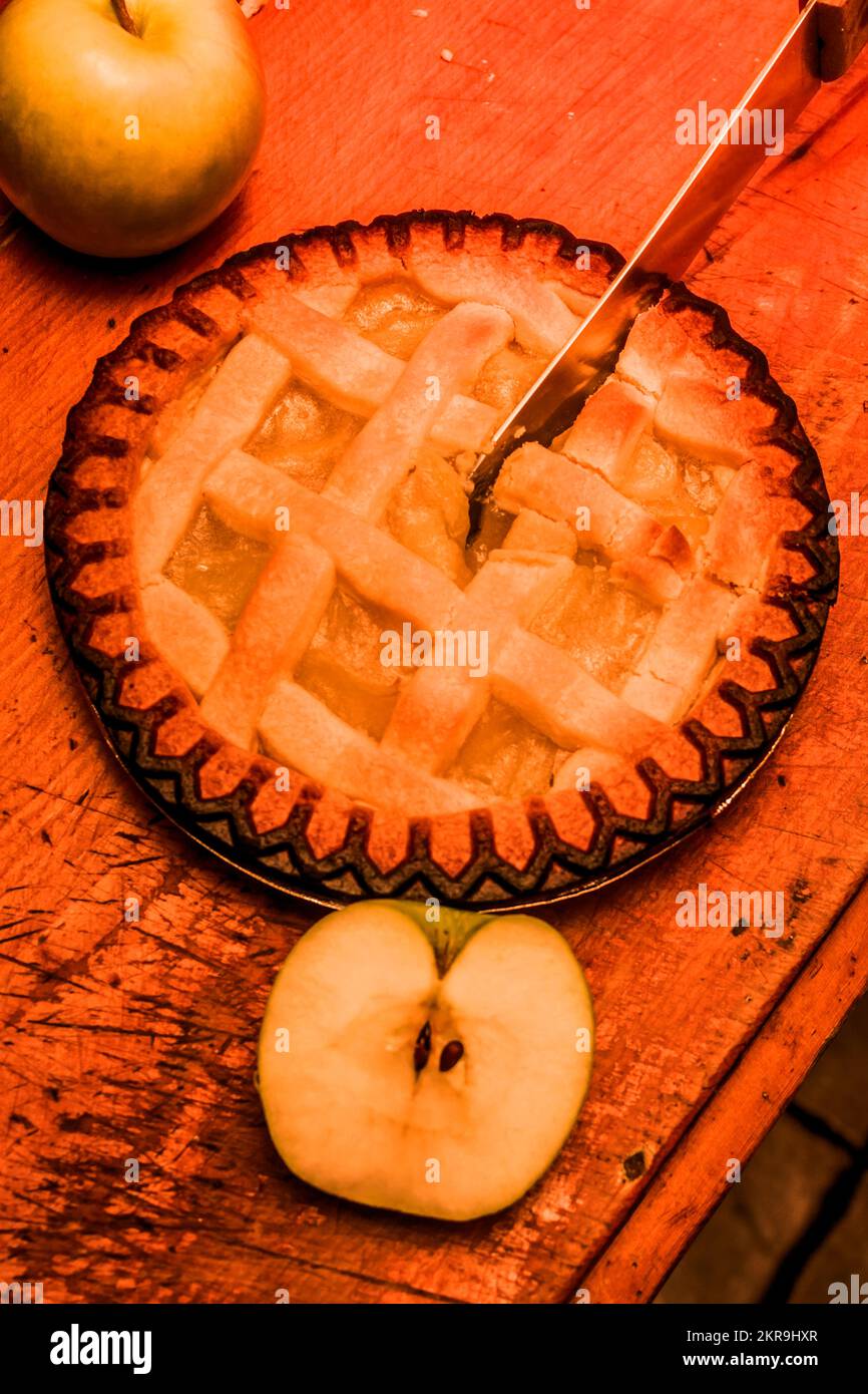 Dessert still life picture on a apple pie being sliced by knife next to
