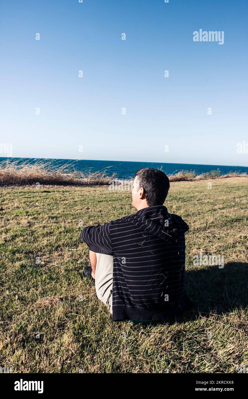Man in late twenties early thirties relaxing on grass hill at the cliffs overlooking the Bass Strait ocean in Devonport, Tasmania, Australia Stock Photo