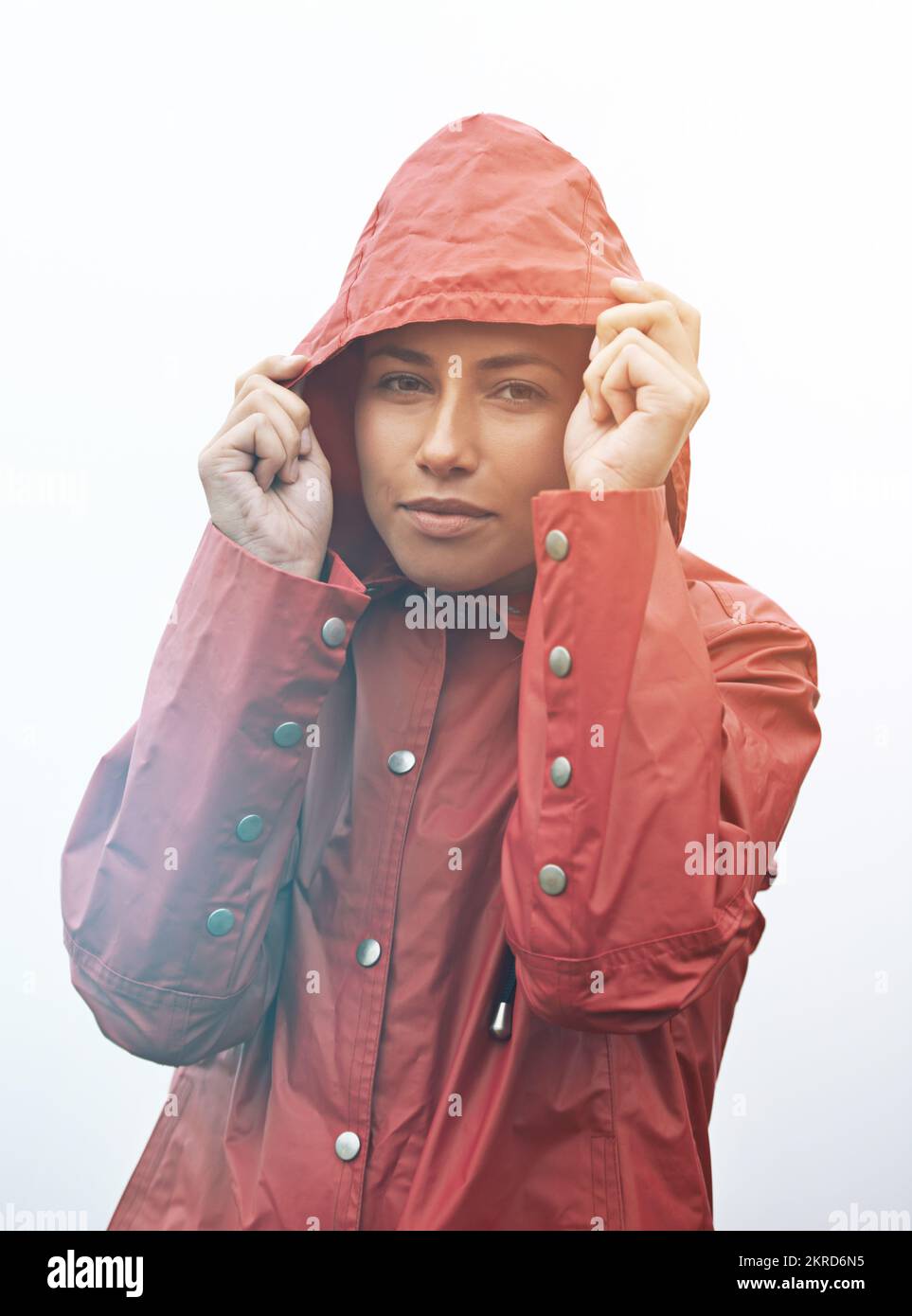 Caught in the rain. Cropped portrait of a young young woman pulling up her hood while standing in the rain. Stock Photo