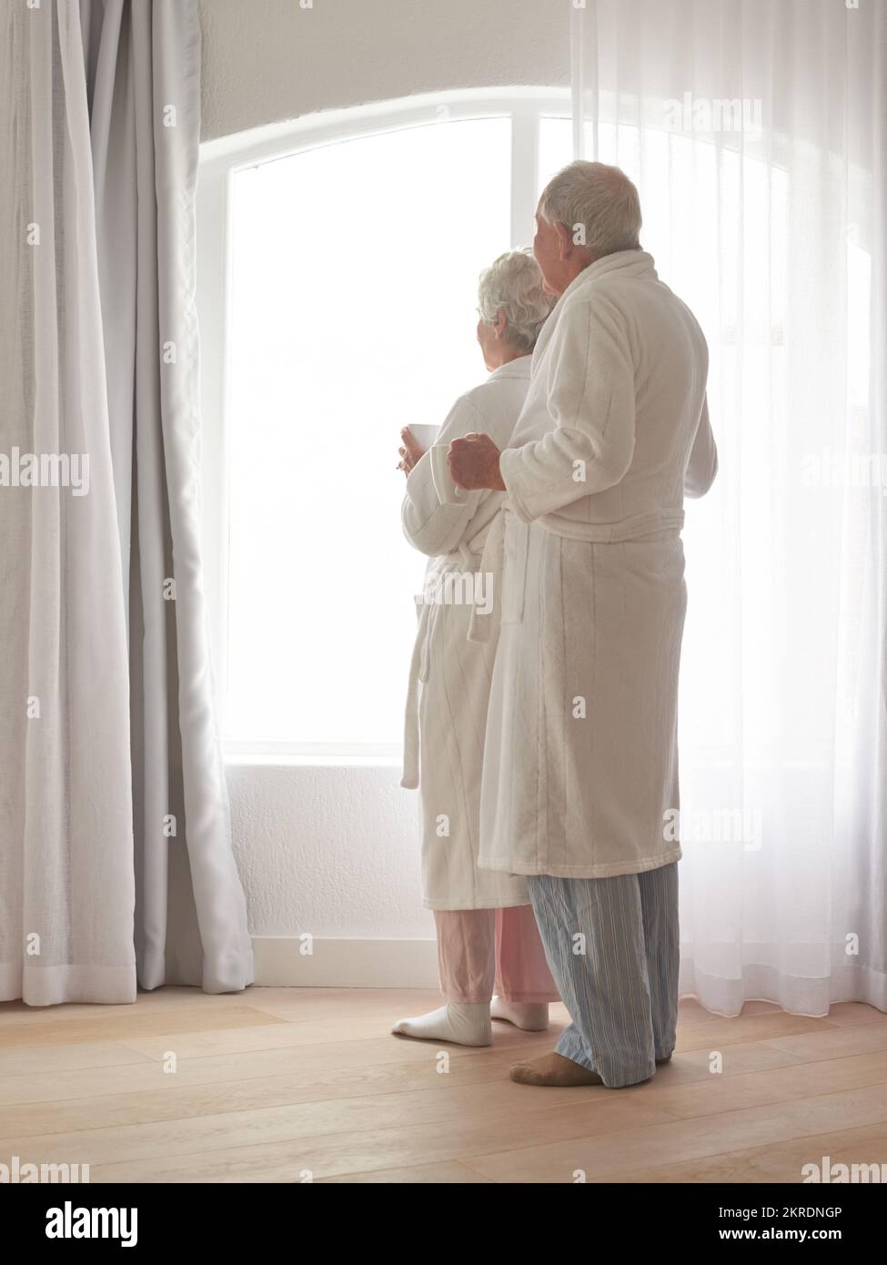 What a beautiful morning. a senior couple in bathrobes looking out of a window. Stock Photo