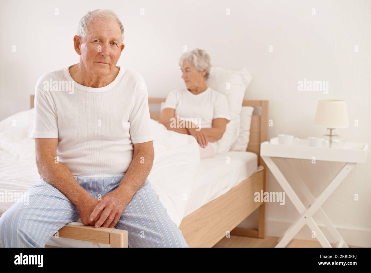 Feeling sad this morning...An elderly man looking unhappy while his wife sits behind him in bed. Stock Photo