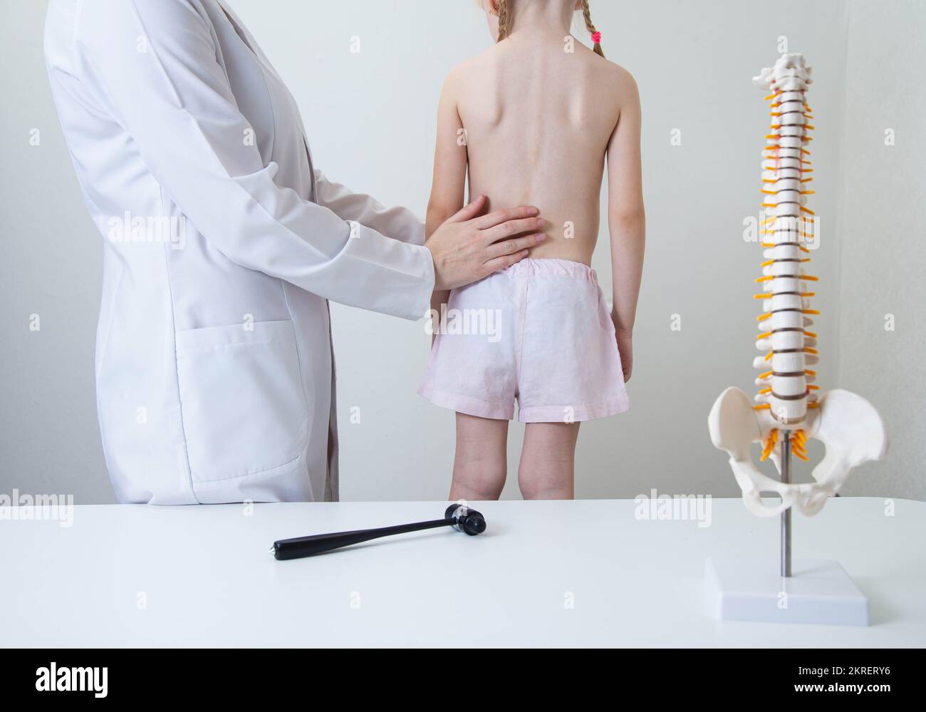 A pediatric neurologist doctor examines the back of a 5-year-old girl who has back pain. Treatment of muscle pain and scoliosis in children, kyphoscol Stock Photo