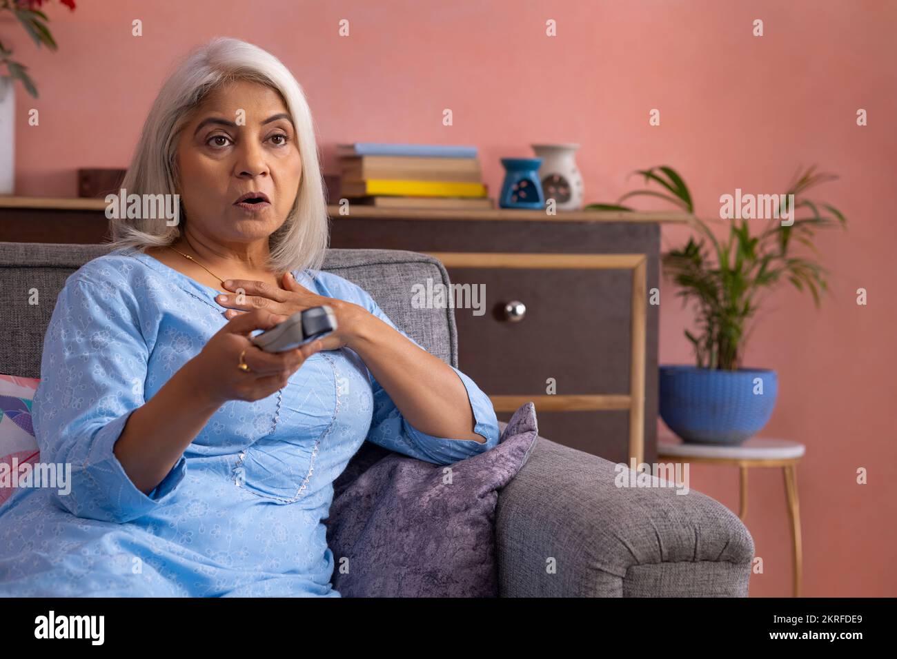 Portrait of a shocked old woman watching TV in the living room Stock Photo