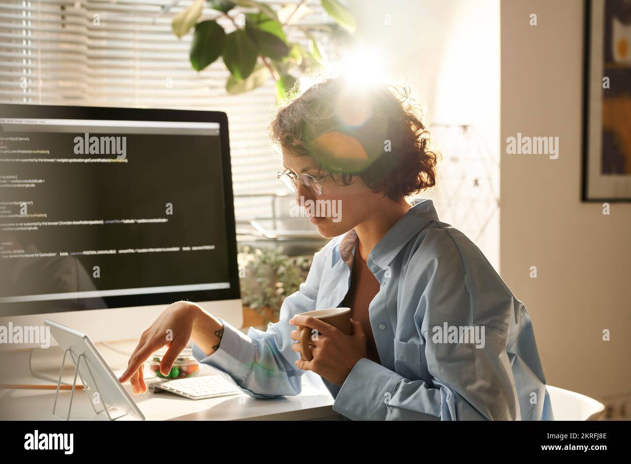 Young IT programmer using tablet pc to work with computer program while working at her workplace at office Stock Photo