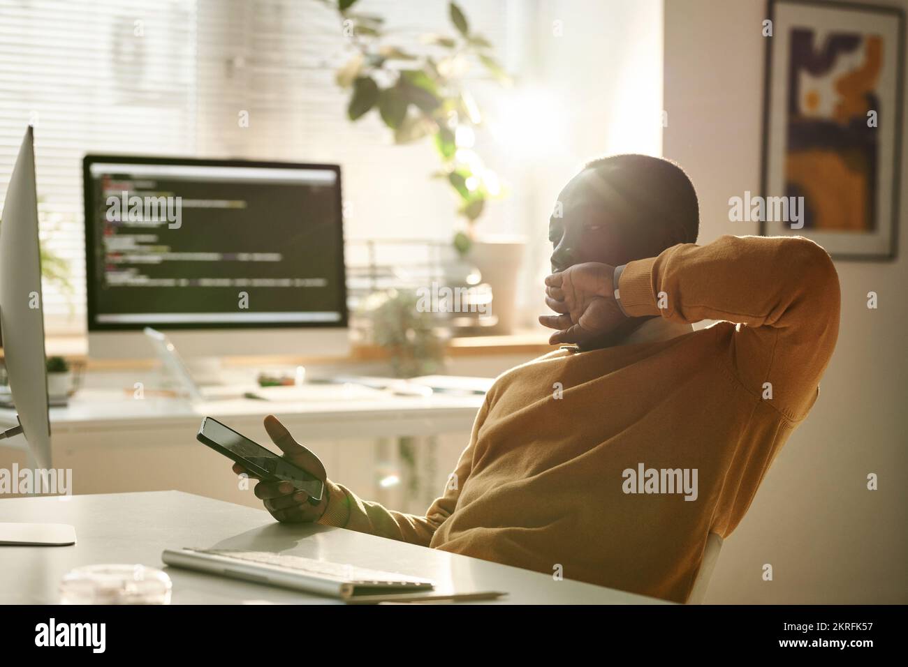 African American tired IT developer using smartphone at work while working at office Stock Photo