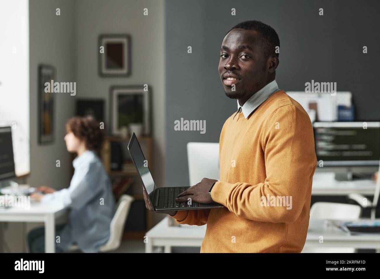 Portrait of African American IT developer looking at camera while working on laptop at IT office Stock Photo