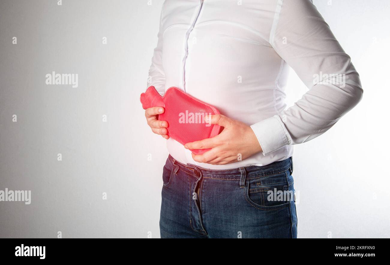A man holds a red heating pad with hot water near his abdomen. Removal of spasms and pains in the abdomen, thermotherapy. Relieve muscle tension Stock Photo