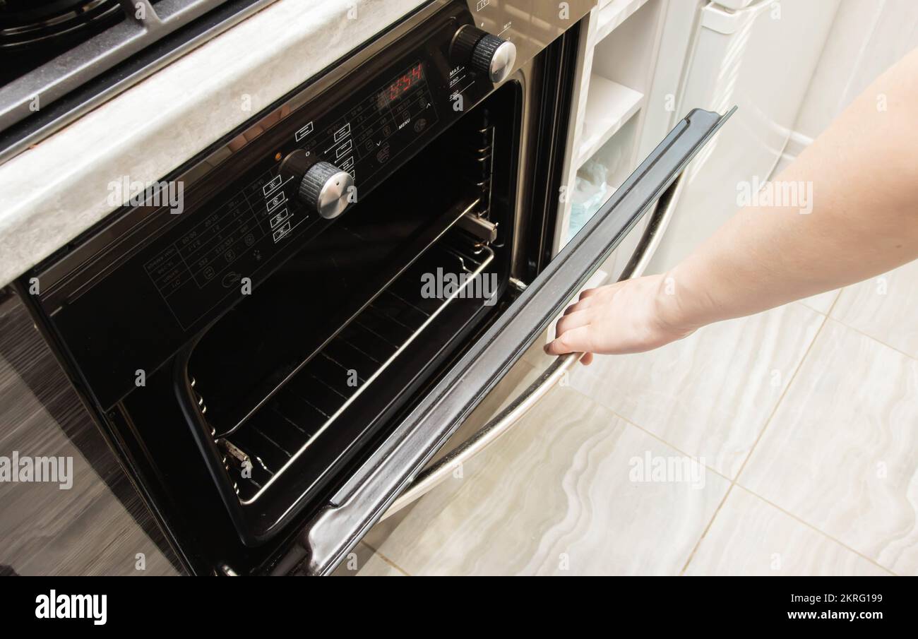 A woman's hand opens the door of a modern oven in the kitchen