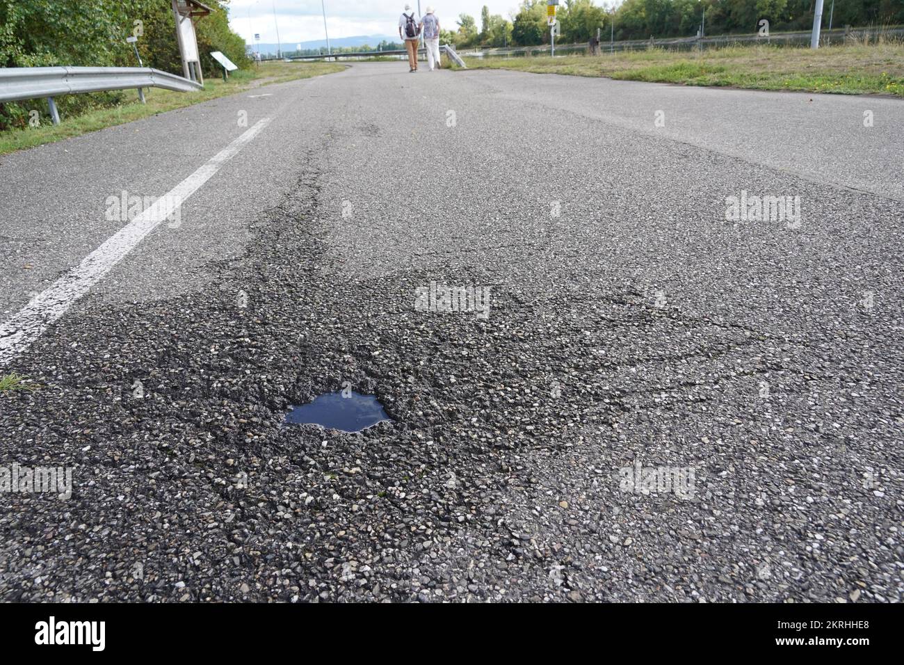 Asphalt road with a small pothole full of rainwater in low angle view. Stock Photo