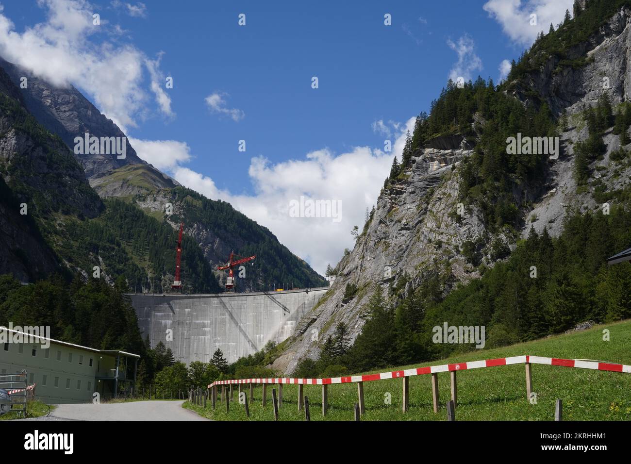 Road to huge grey wall of Gigerwald Dam which stands between rock faces of the Ringelspitz massif. Stock Photo